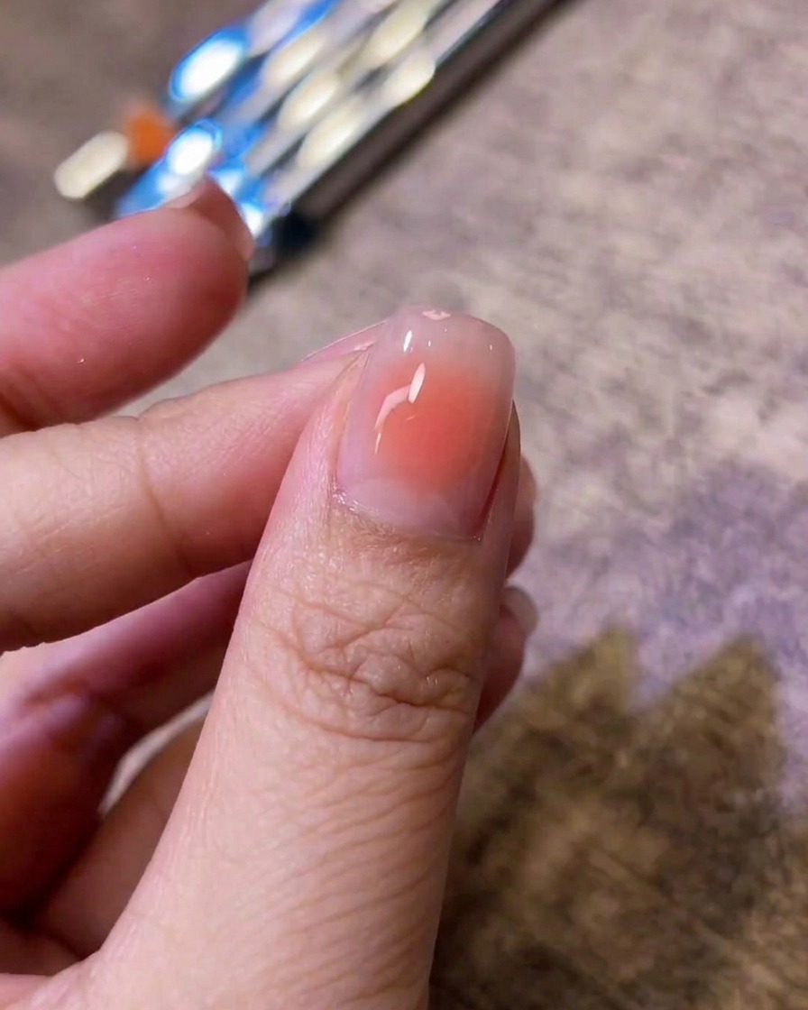 A close-up of a glossy fingernail featuring a softly blended pink blush center over a nude base.