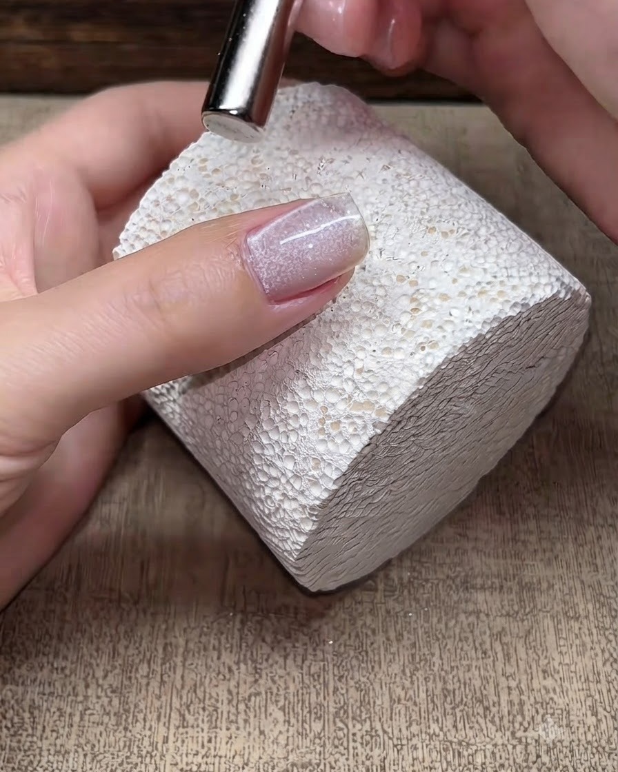 A small magnet tool hovering over a wet cat-eye gel nail to manipulate the magnetic shimmer particles.