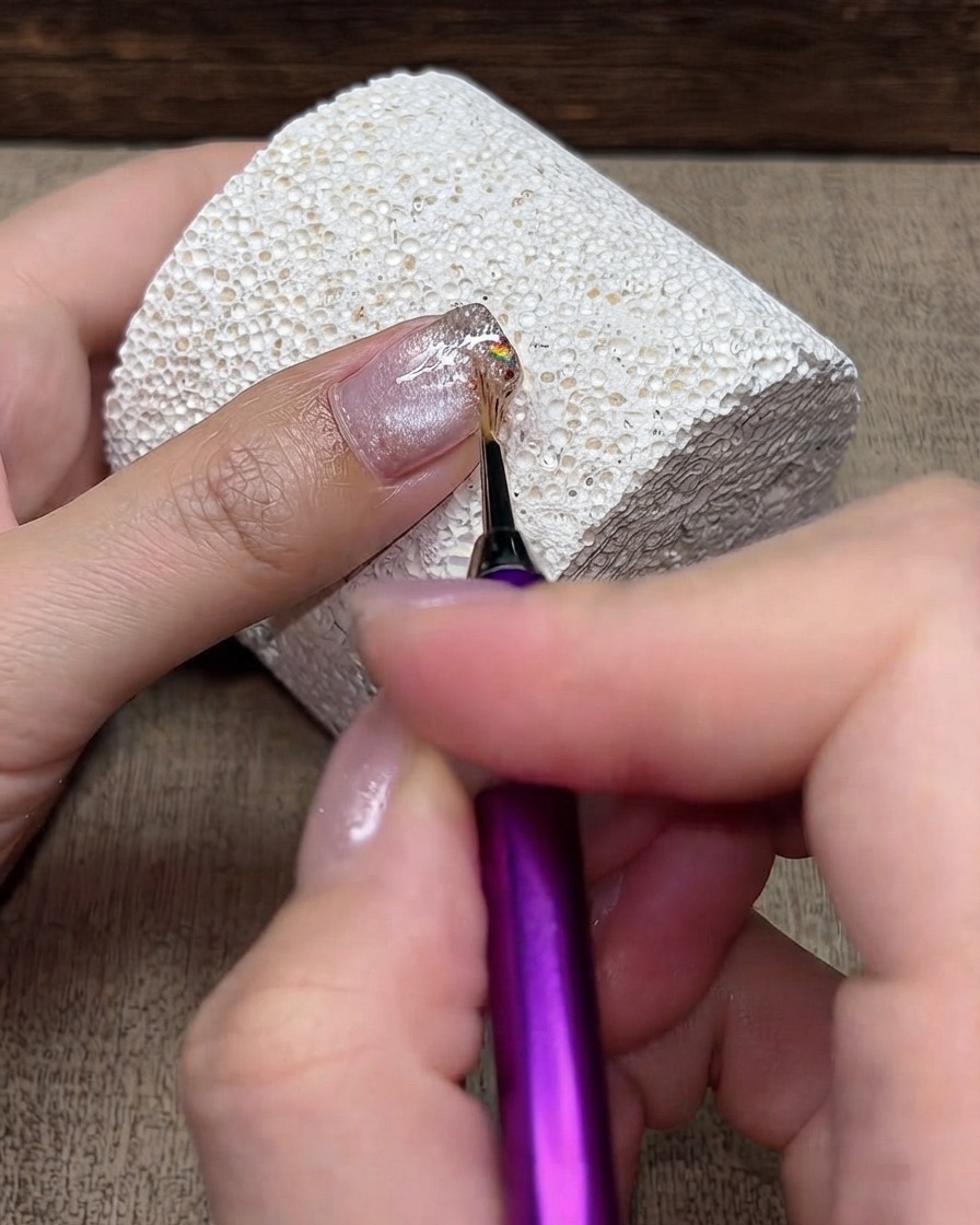 A fine detailing brush lightly feathering glitter particles backward from the tip toward the cuticle.
