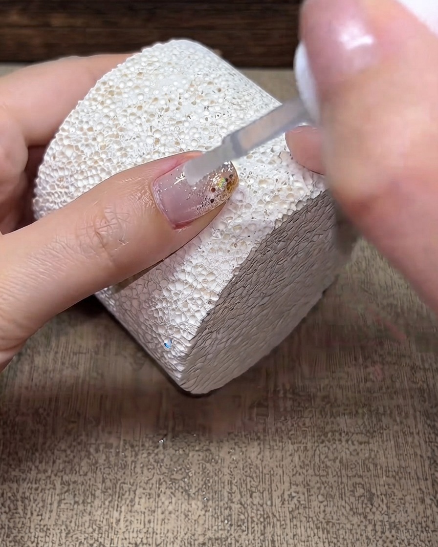 A brush applying a clear layer of builder gel over a decorated nail surface.