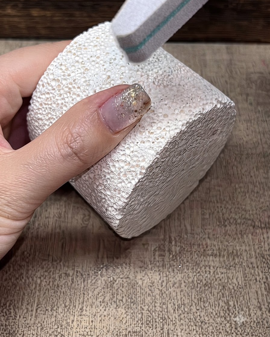 A sponge buffer file smoothing the surface of a manicured fingernail.