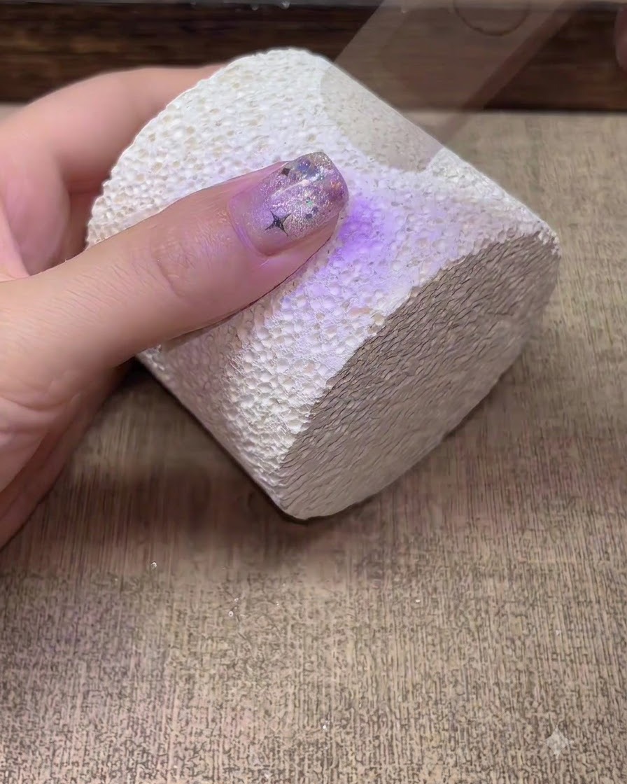 A hand curing under a purple UV LED nail lamp.
