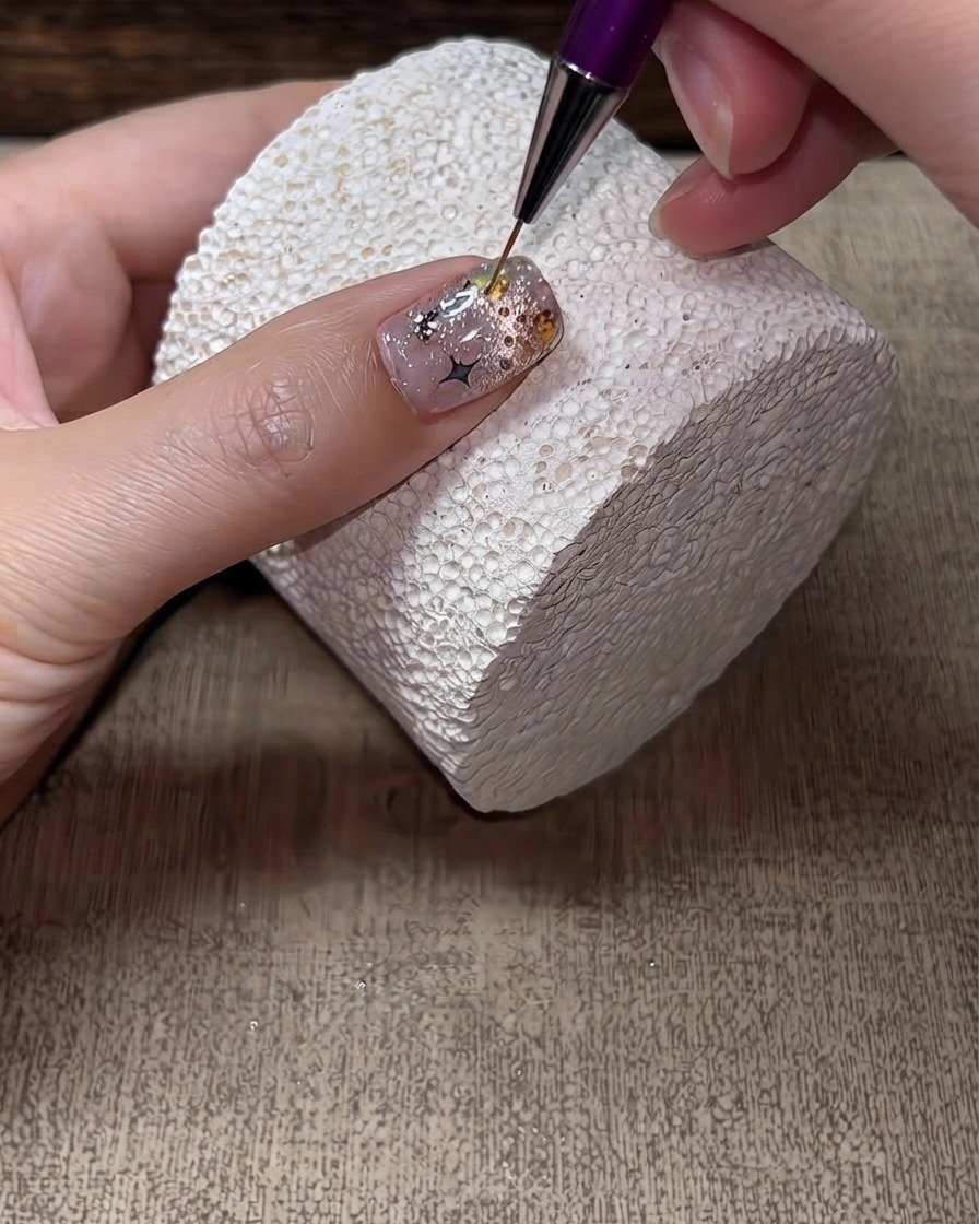 A fine liner brush applying hard top coat around the edges and gaps of rhinestones on a finished nail.