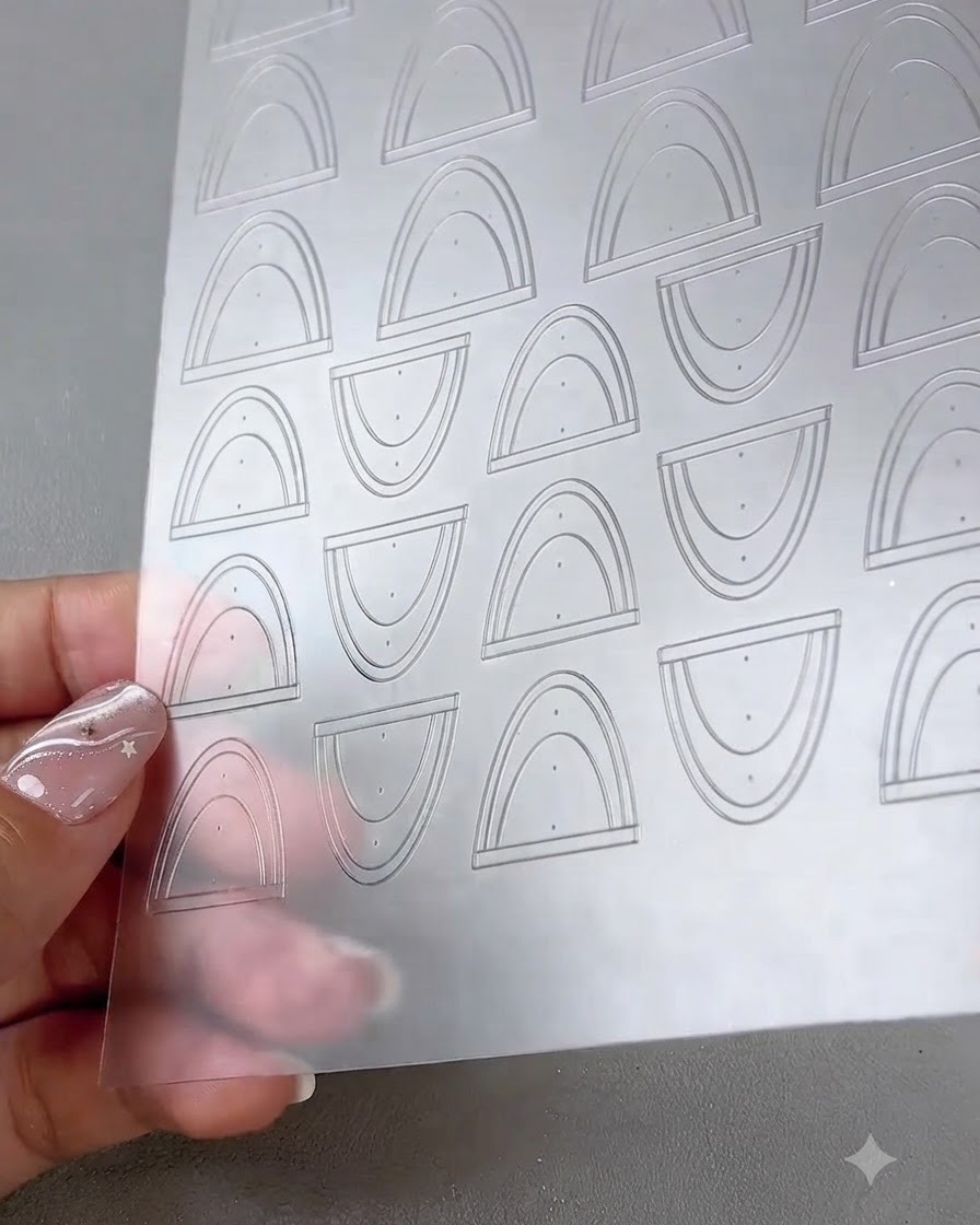 A close-up view of a clear sheet containing multiple curved French tip and line art stickers.