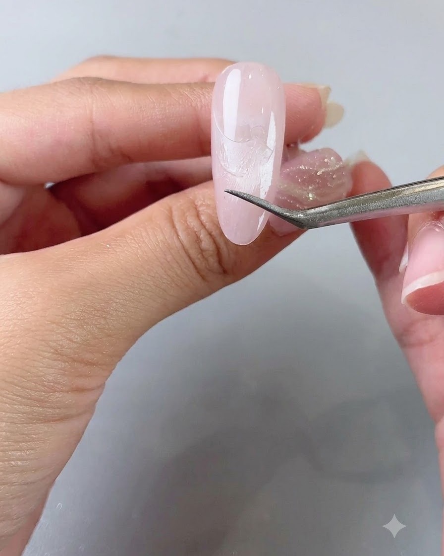 Tweezers gently peeling off a French guide sticker, revealing a clean line on the nail.