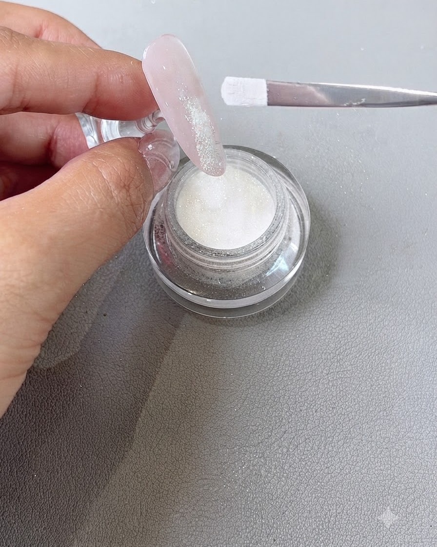 Dipping powder being sprinkled from a brush onto the wet gel tip area of a fingernail.