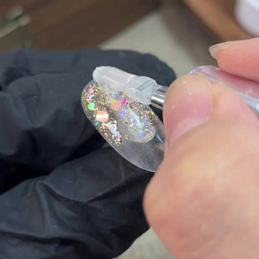 A brush applying clear base gel over a cured glitter layer on a nail.