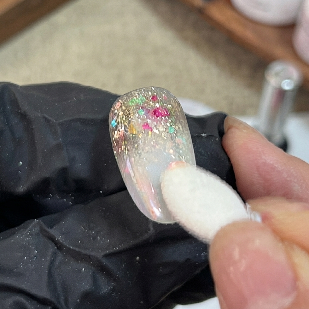 A sponge applicator dabbing iridescent aurora powder onto the gradient section of a decorated artificial nail.