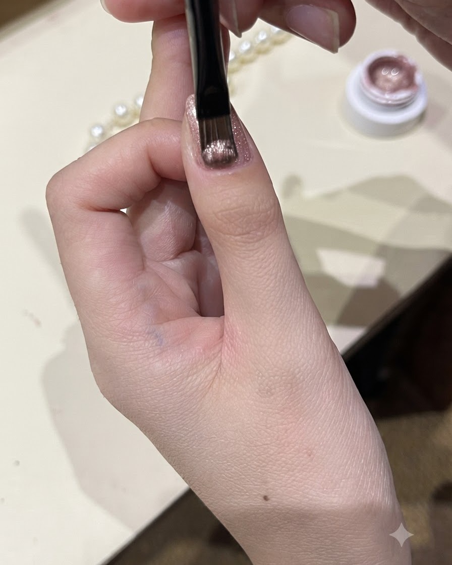 A close-up view of a fine brush applying a shimmering cat-eye gel polish onto a thumbnail.