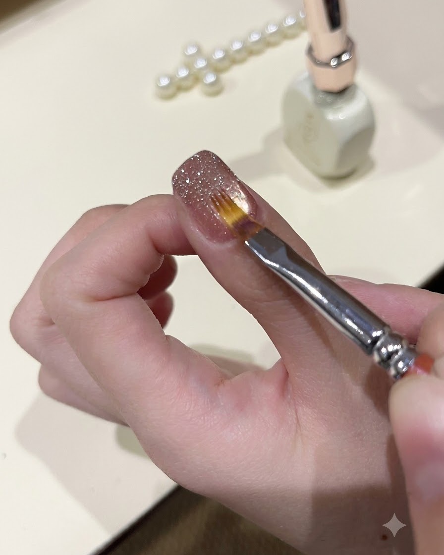 A fine brush smoothing out sparkly glitter gel on the surface of a manicured nail.