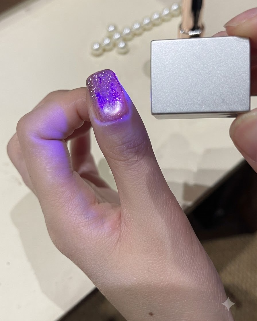 A close-up view of a thumb under a small handheld UV LED light curing the gel polish.