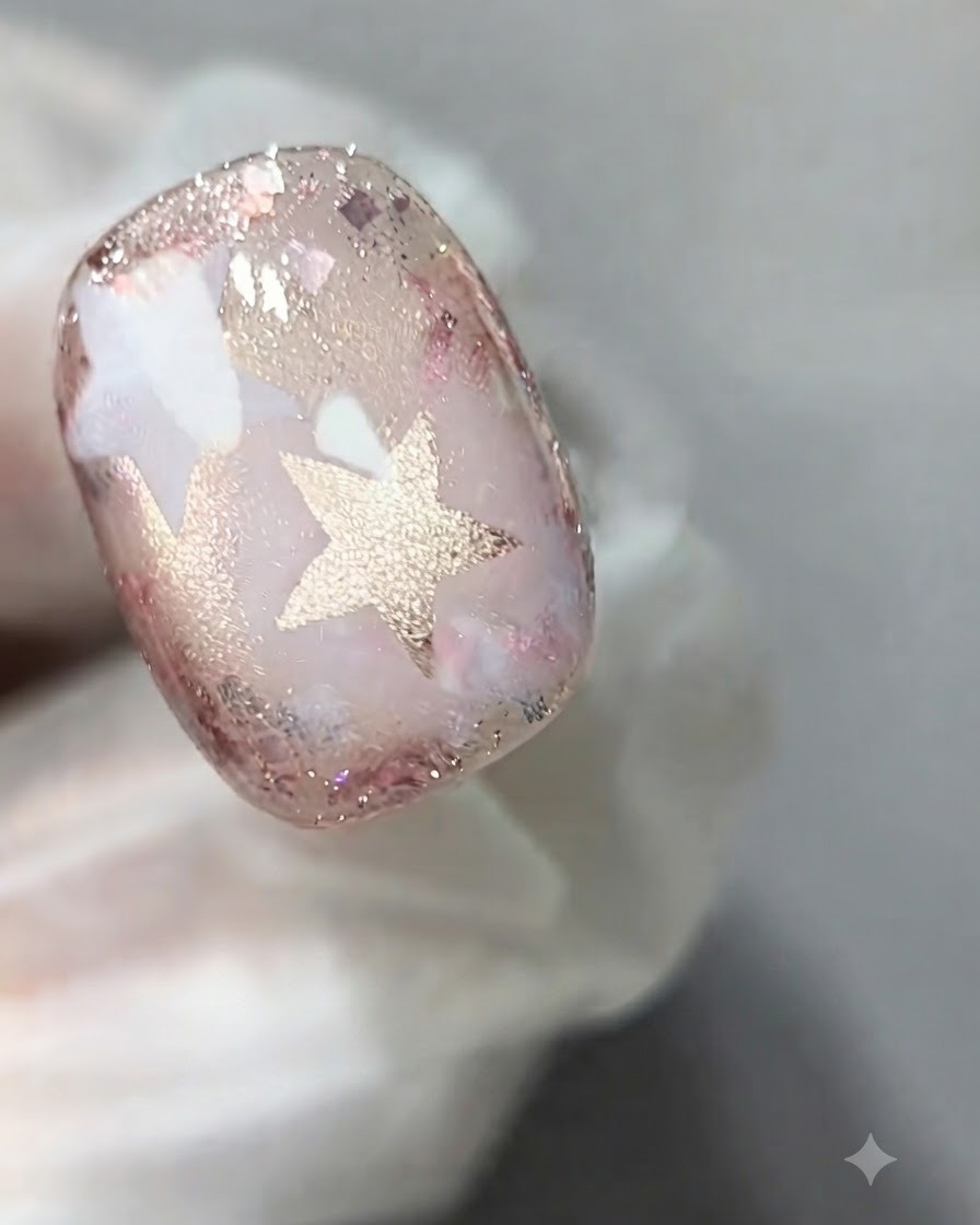 A nail brush applying a coat of sheer pink cat-eye gel onto the surface of a decorated nail.