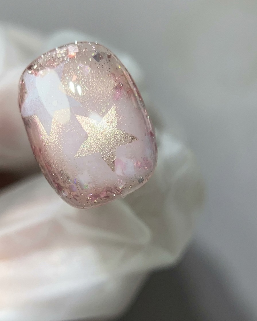 A magnetic wand held over a pink cat-eye gel nail to concentrate the shimmering reflection into a glass bead effect.