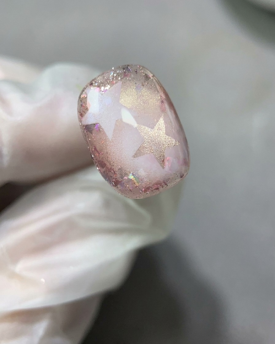 A nail brush spreading a smooth, thin layer of clear base gel over the completed star and glitter nail design.