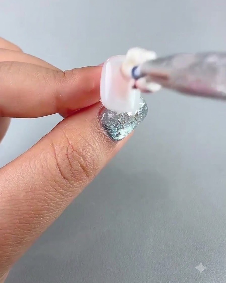 A detailed view of a brush applying a pinkish patting gel to the center of a nail.