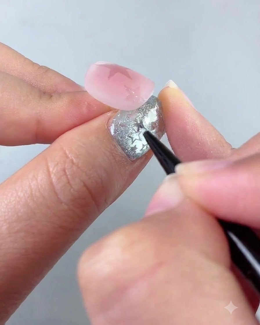 A liner brush detailing a smaller star shape near the bottom left corner of a pink nail.