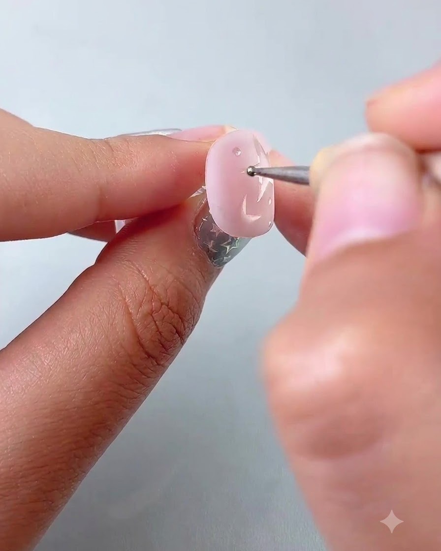A dotting pen placing small accent dots around painted stars on a pink nail.