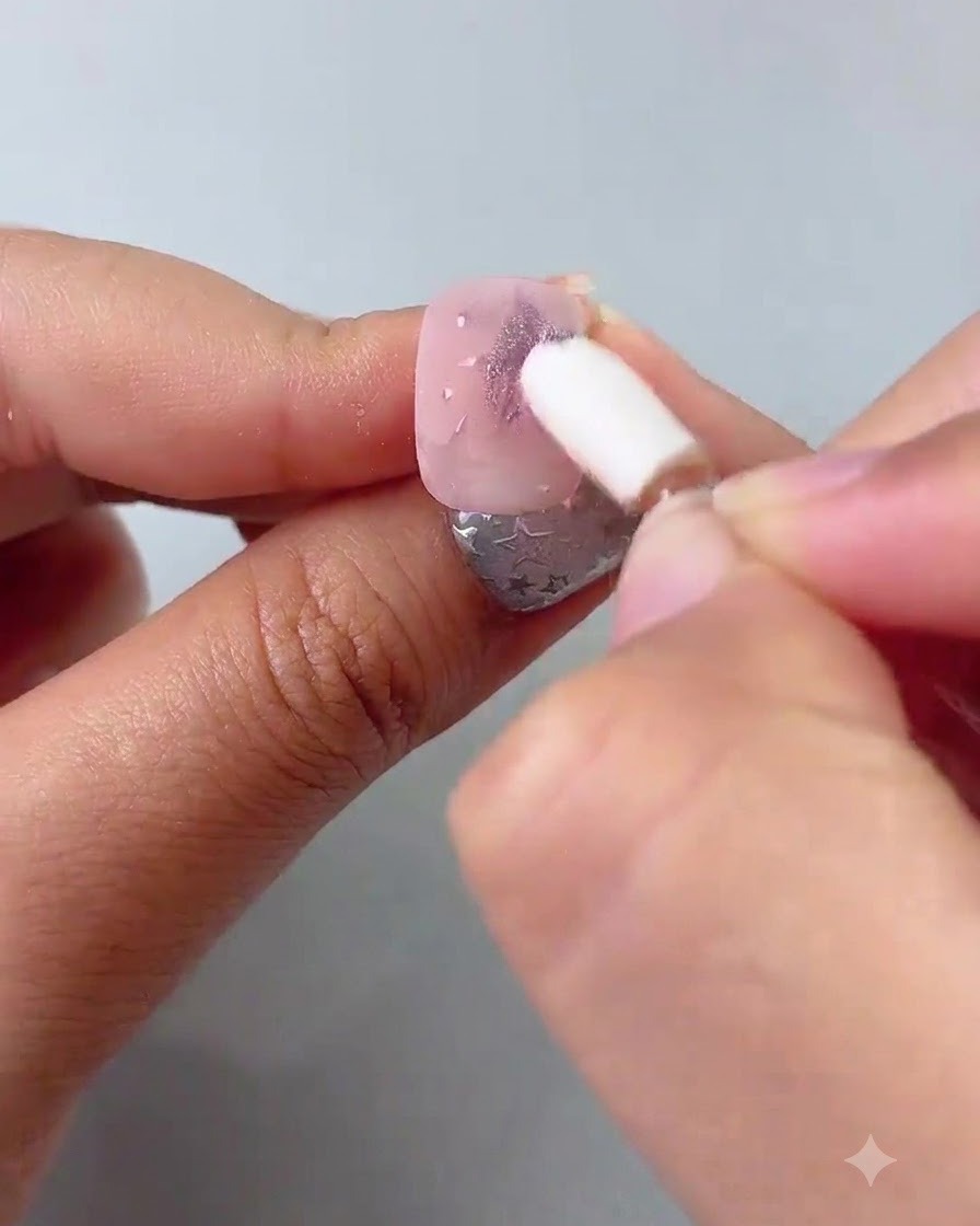 A silicone sponge applicator rubbing purple chrome powder onto painted stars on a nail.