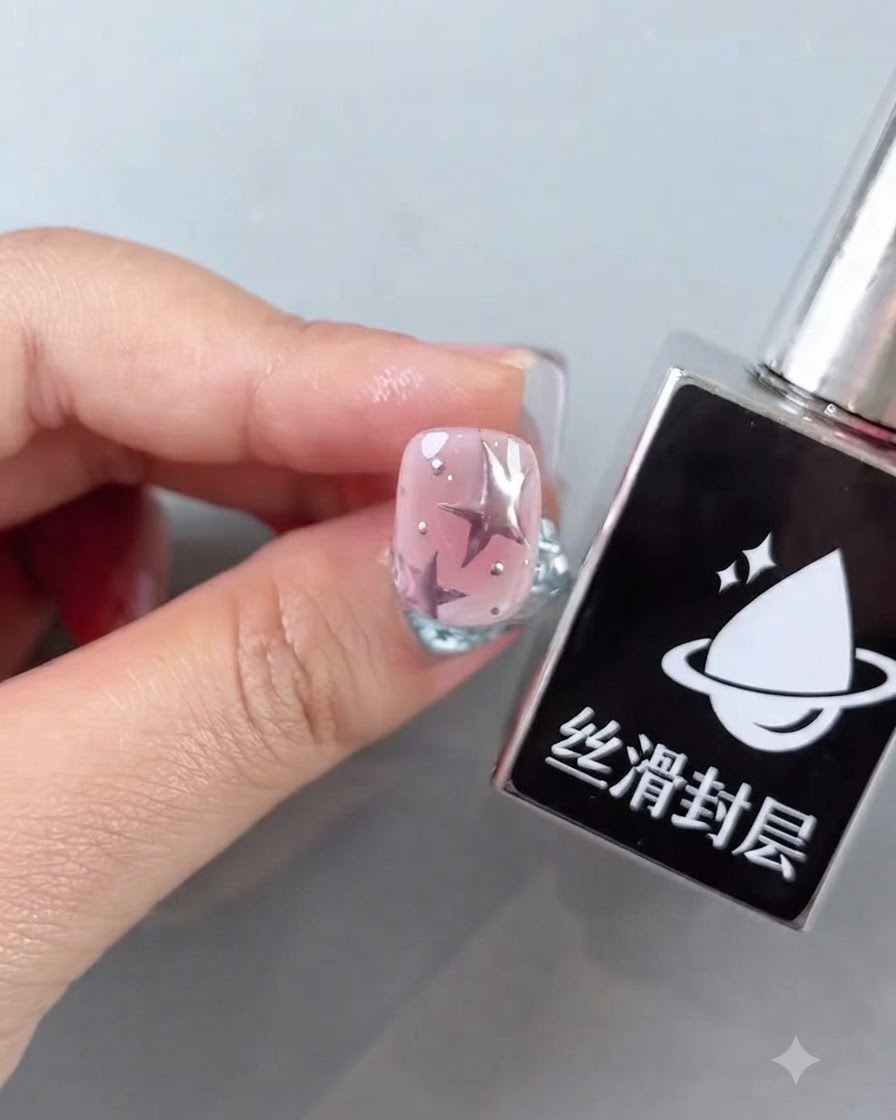 A bottle of smooth top coat next to a finished pink nail featuring star designs and shiny silver accents.