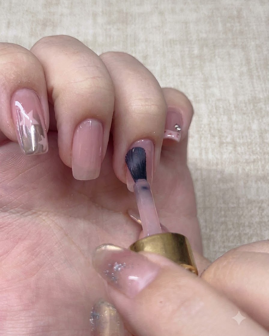 A brush applying a second layer of nude base polish onto the nail.