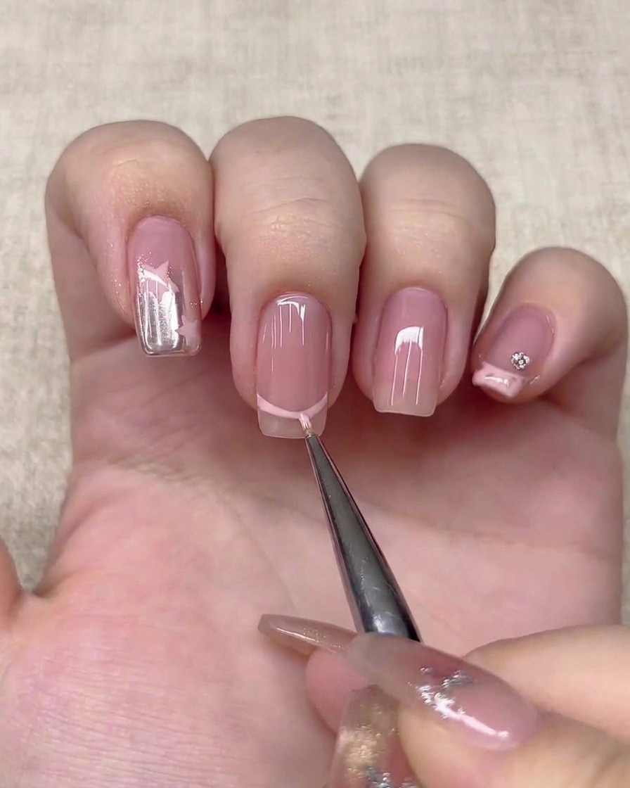 A fine liner brush drawing a light pink French tip line on a nail.