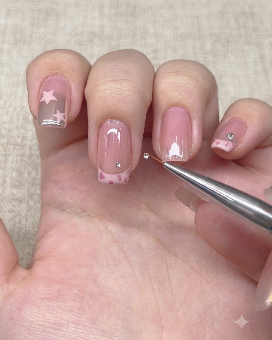 A detail tool placing a small rhinestone above the French tip line on a nail.