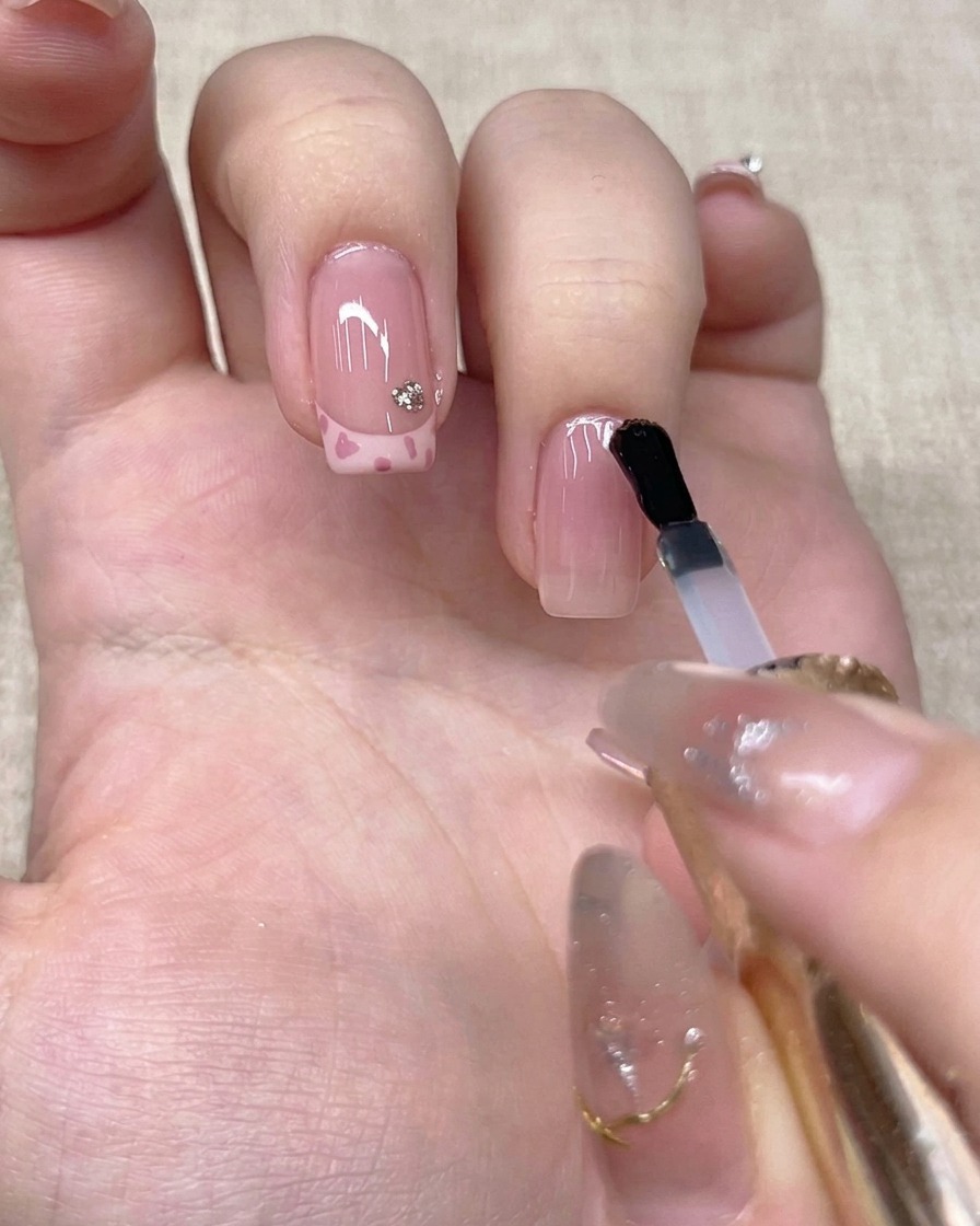 A brush applying a clear top coat onto the nail of a ring finger.