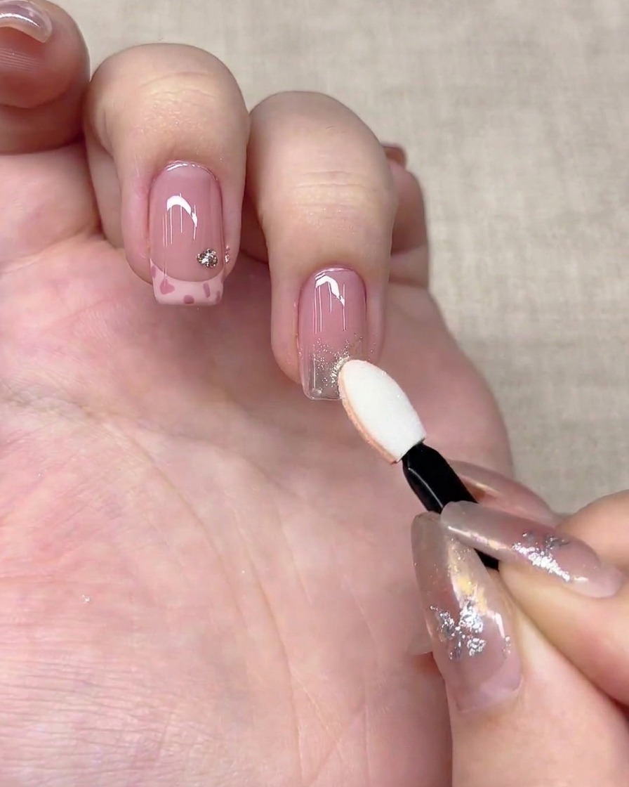 A sponge eyeshadow applicator pressing silver chrome powder onto the tip of a fingernail.