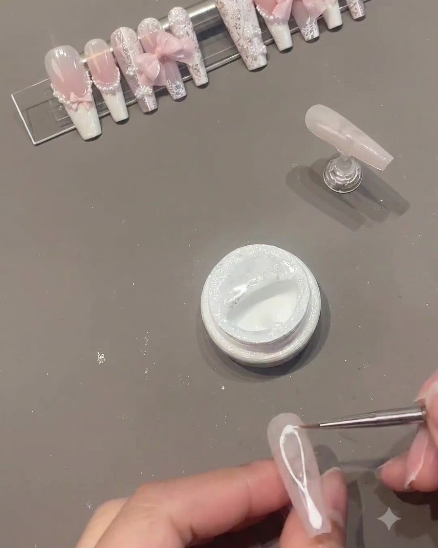 A fine liner brush drawing white spider gel lines across the middle of a pink gel nail.
