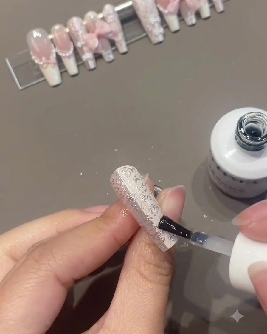 A nail brush applying clear or top coat over a intricately decorated floral nail while other finished nails are displayed on a stand in the background.
