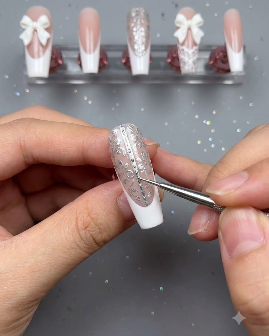 A fine detail brush and tweezers being used to place tiny pearl accents down the center line of a decorated floral press-on nail.