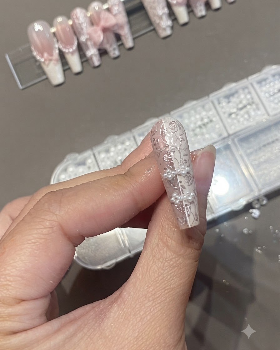 A nail brush applying a clear top coat over a textured nail design featuring pearls and lace stamping.