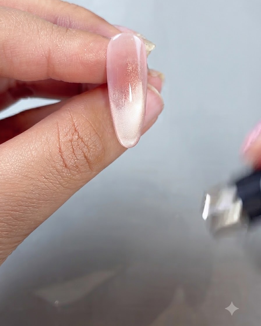A magnetic wand being held near a painted fingertip to shape the cat-eye shimmer into a French tip style.