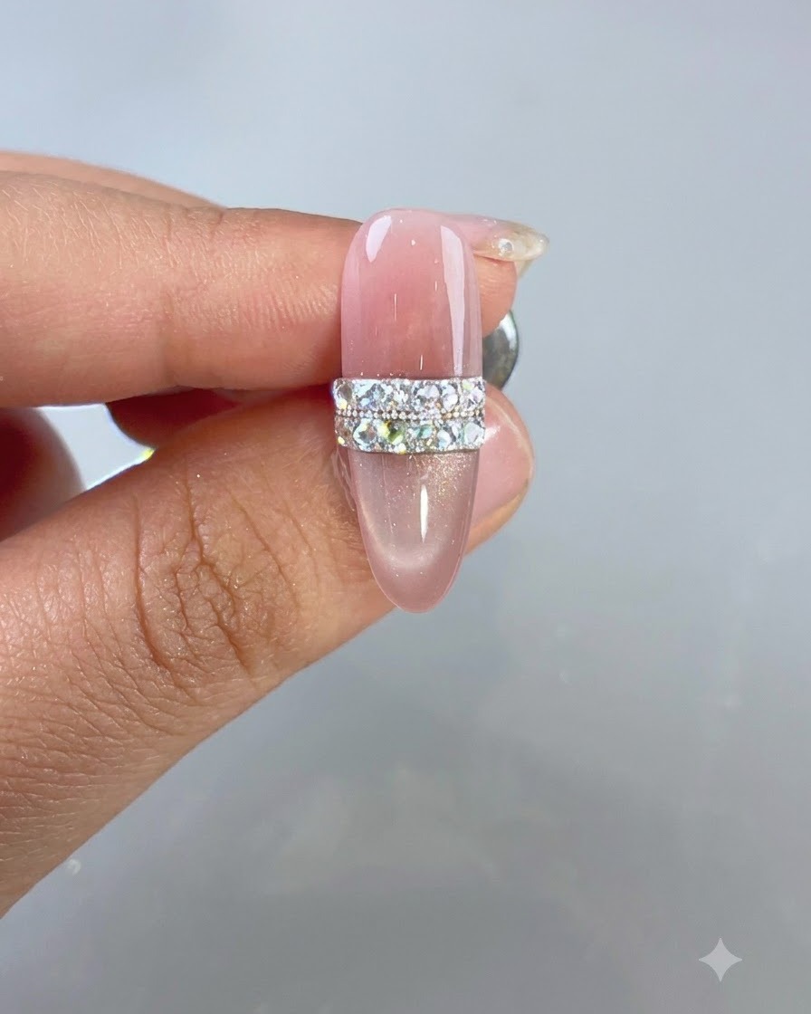 A completed pink cat-eye nail design featuring a sparkling rhinestone and bead ring motif under studio lighting.