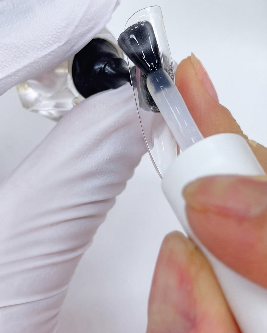 A brush applying a top coat layer onto a clear nail display stand.