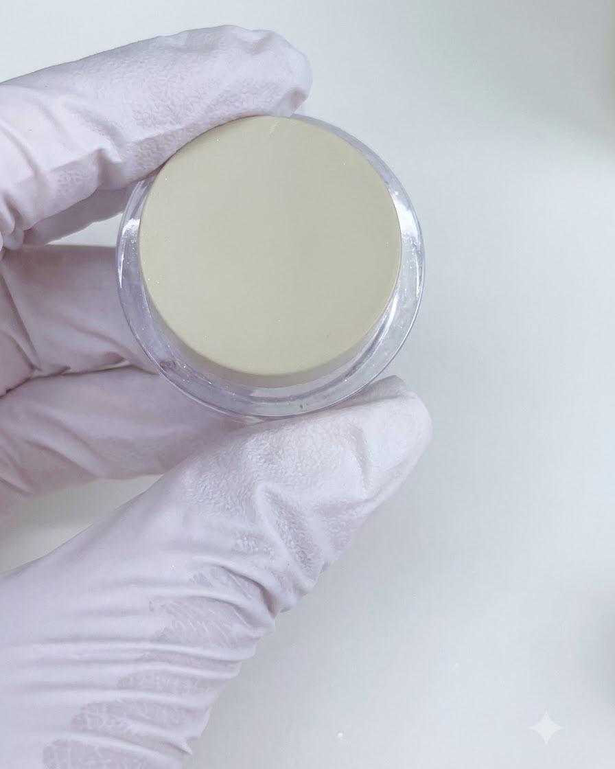 A close-up view of a gloved hand holding a jar of pearl powder while preparing to apply it to a nail.