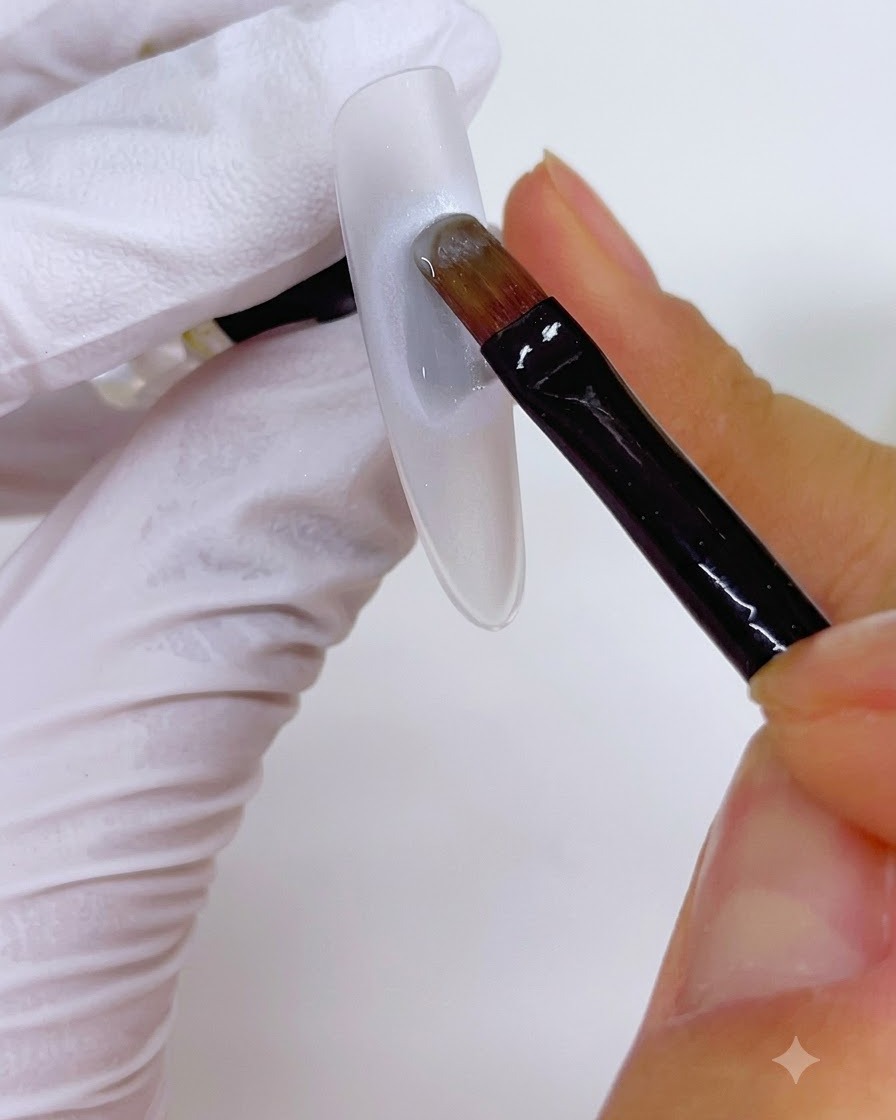 A brush applying a coat of gel over a circular pearl base on a nail.