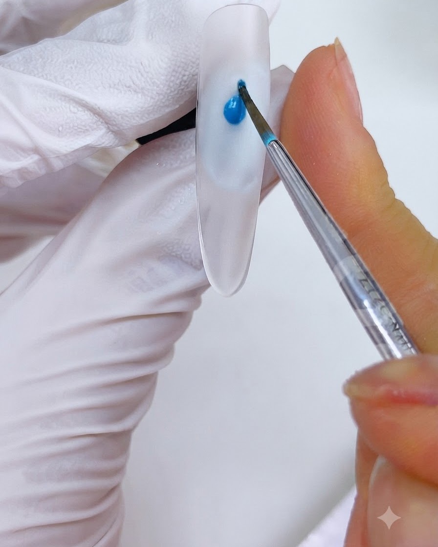 A fine brush placing a drop of sky blue ink onto a nail design.
