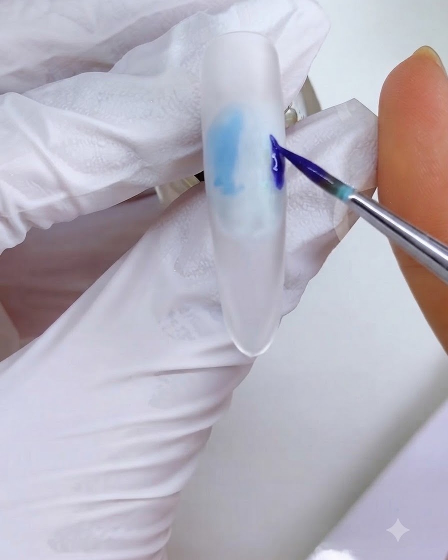 A fine liner brush applying a blue-purple ink block onto the right side of the white frosted nail surface.