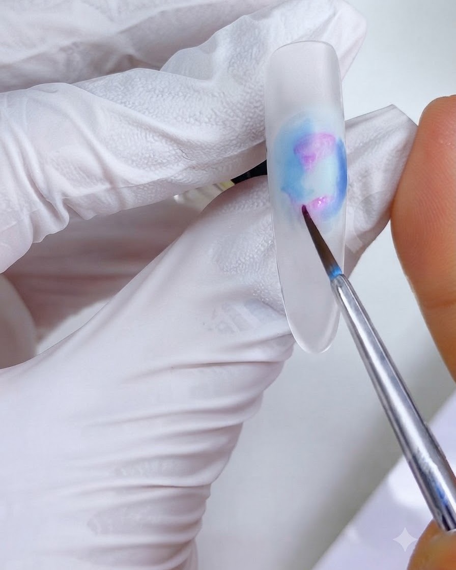 A fine detail brush applying small pinkish-magenta ink dots onto the left upper and lower regions of the nail design.