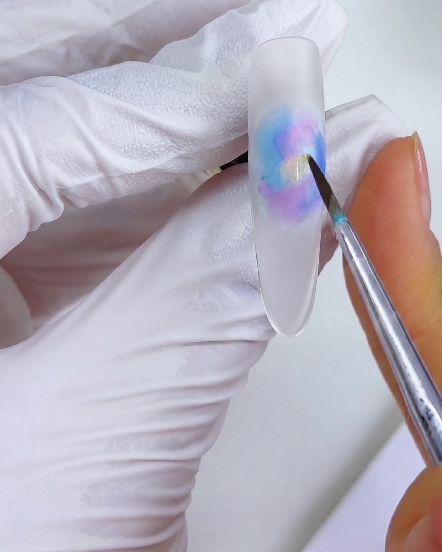 A fine brush placing a dab of orange ink into the middle of the watercolor blooming pattern.