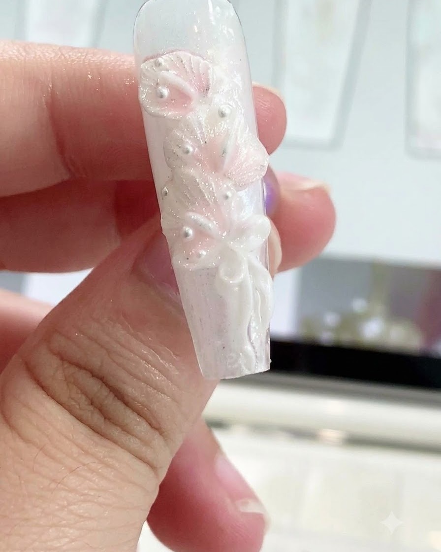 A silicone shaping pen smoothing a bow knot onto a sculpted nail design.