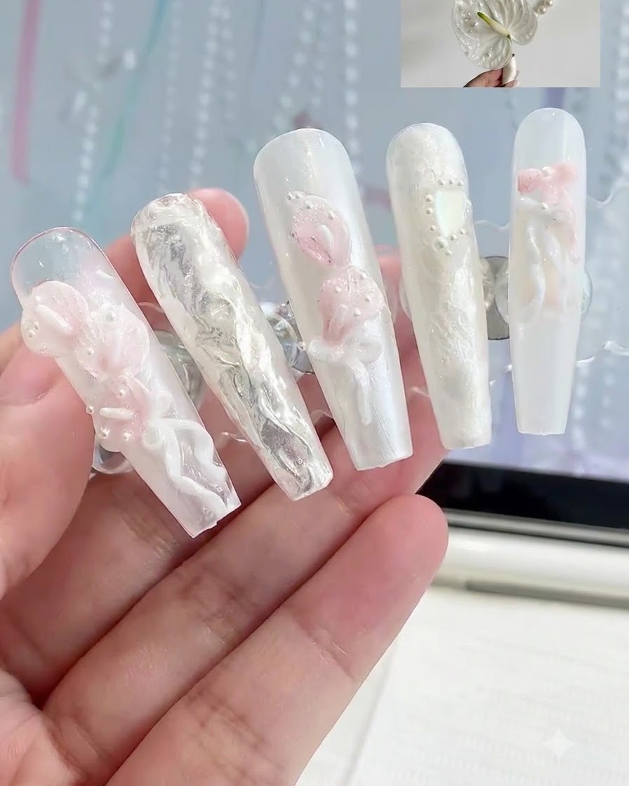 A display stand holding multiple press-on nails with various 3D white and pink floral nail art designs.