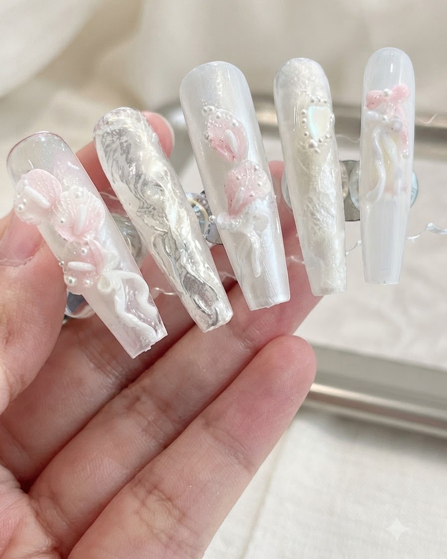 A display of finished press-on nails featuring 3D calla lilies, bows, and pearl embellishments on a neutral background.