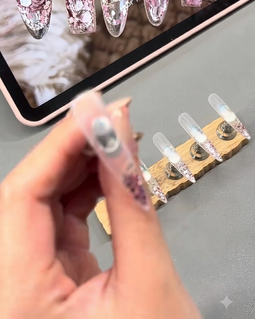 A close-up view of clear gel being applied over glitter flakes on a nail.