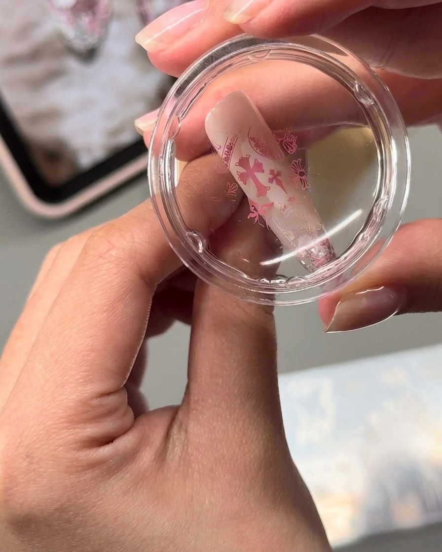 A clear jelly stamper transferring pink stamped nail art designs onto an almond-shaped nail surface.