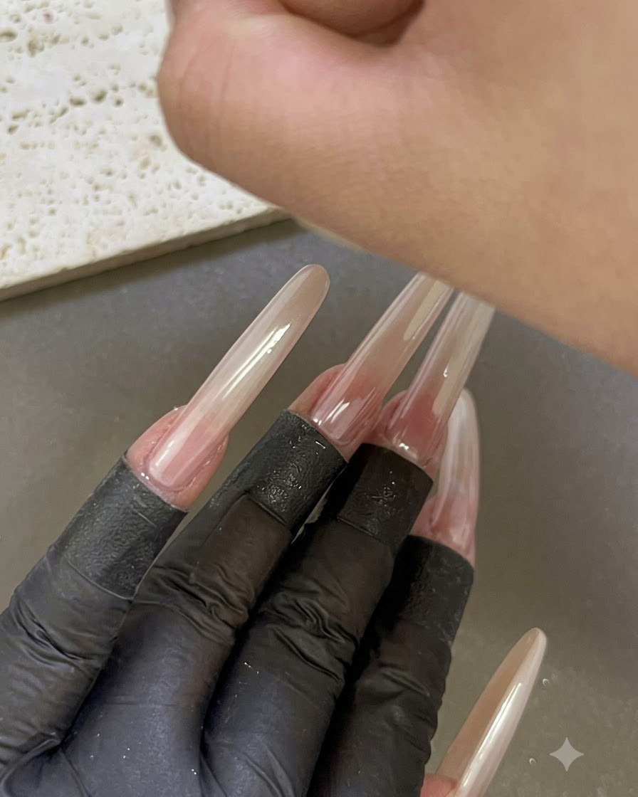 A hand placed under a UV/LED nail lamp with other manicured extended fingers visible in the foreground.