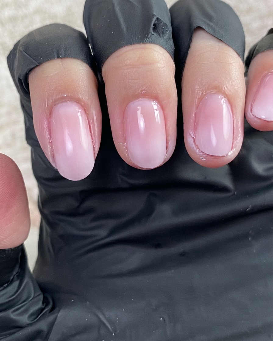 A close-up view of a fresh coat of clear base gel glistening on the surface of prepped nails.