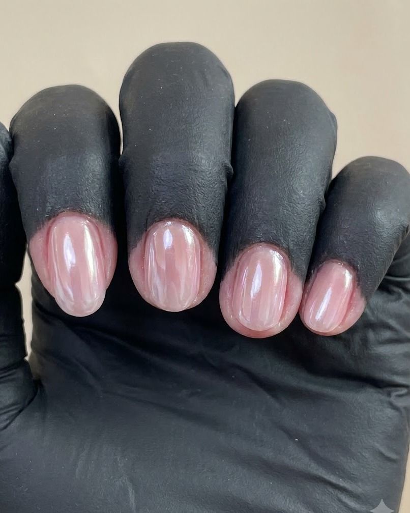 A close-up view of a gloved hand showing four manicured nails with a glossy pearl chrome finish against a plain background.