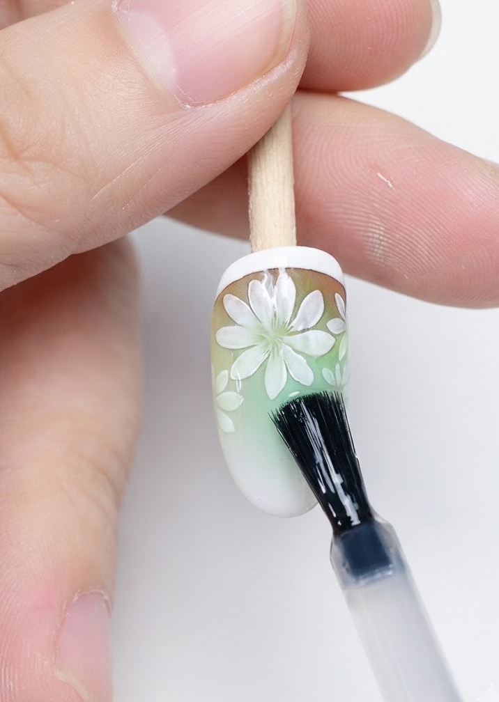 A brush applying matte top coat over completed daisy nail art.